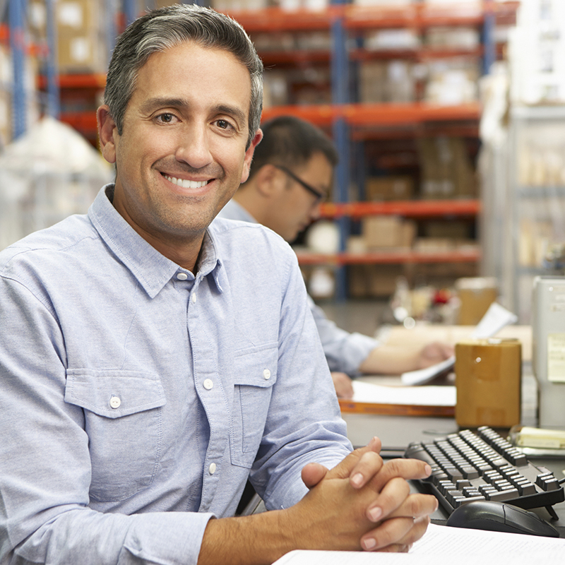 Smiling man seated at a computer in a warehouse.