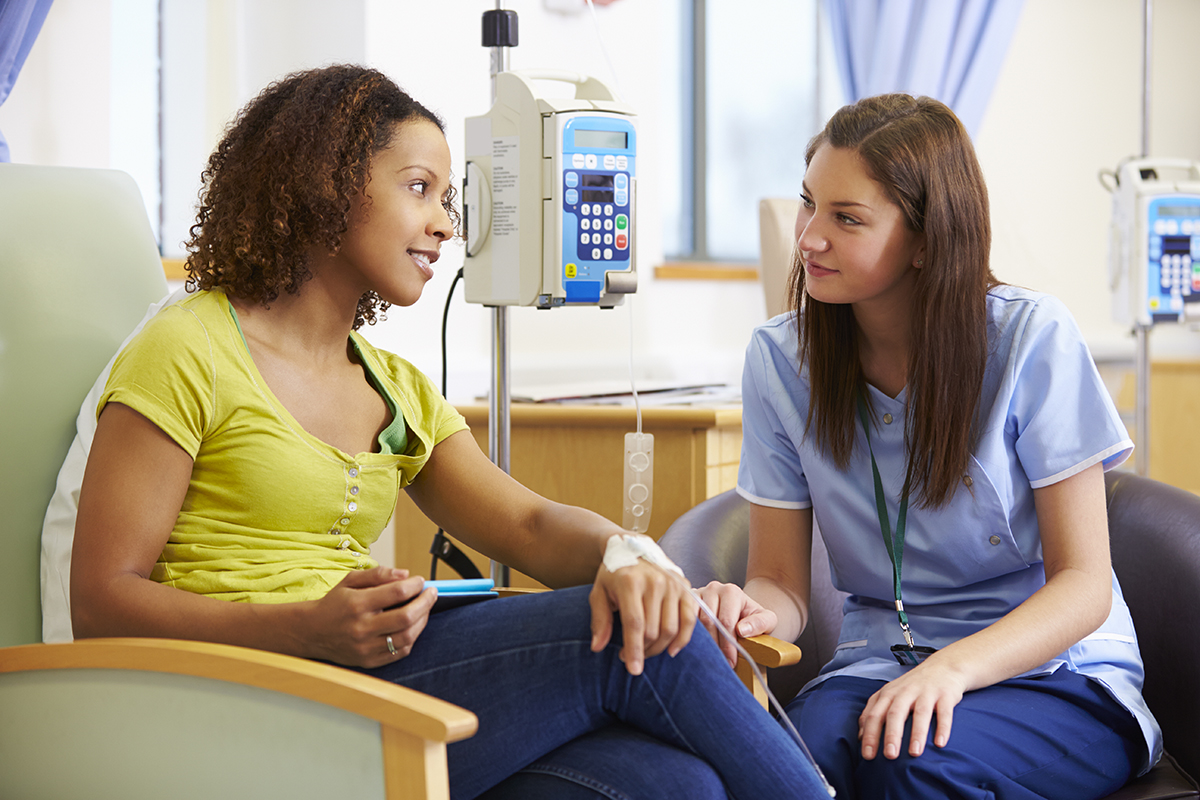 Female patient and female nurse sit looking at each other while the patient has an IV in her hand.