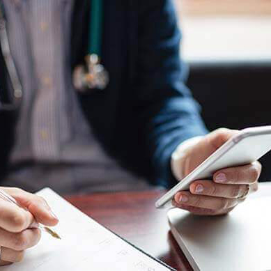 A doctor writing and looking at a phone.