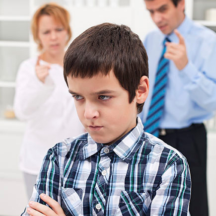 An indignant boy with his arms folded and back turned toward his parents, who are lecturing him.