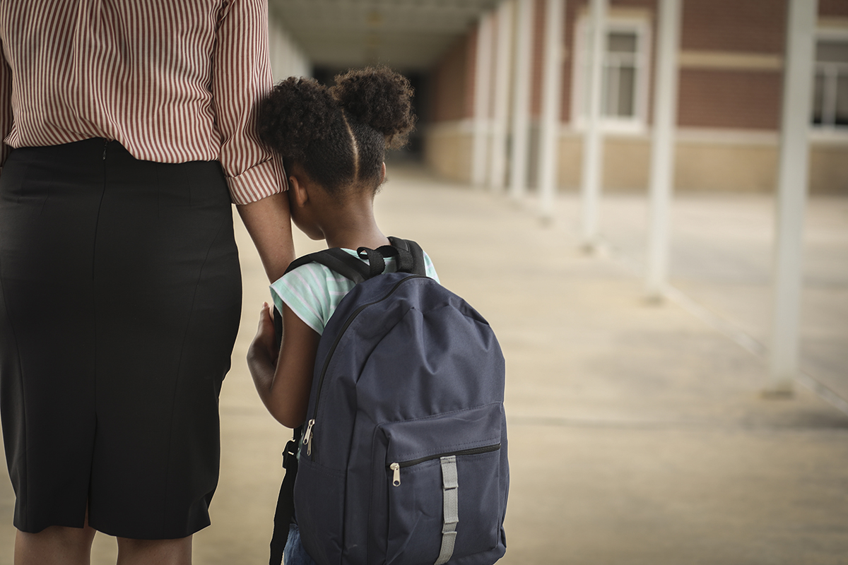 Photo from the back of a child holding tightly to and leaning on a parent's arm.