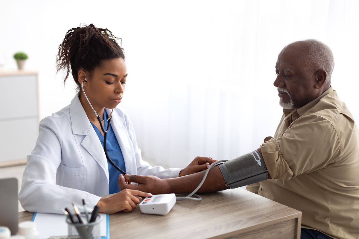 A health care professional takes a blood pressure reading from an older man