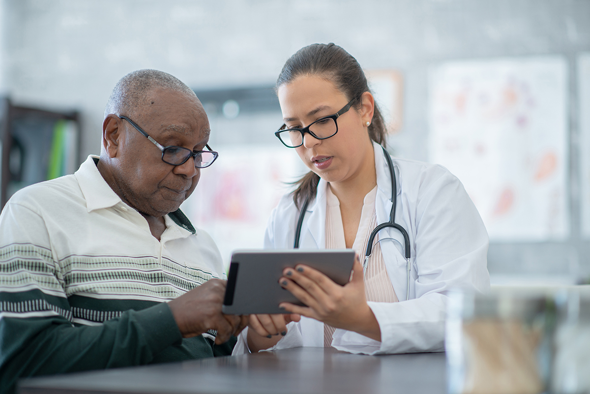 Image of a health care professional showing an older patient something on a tablet device.