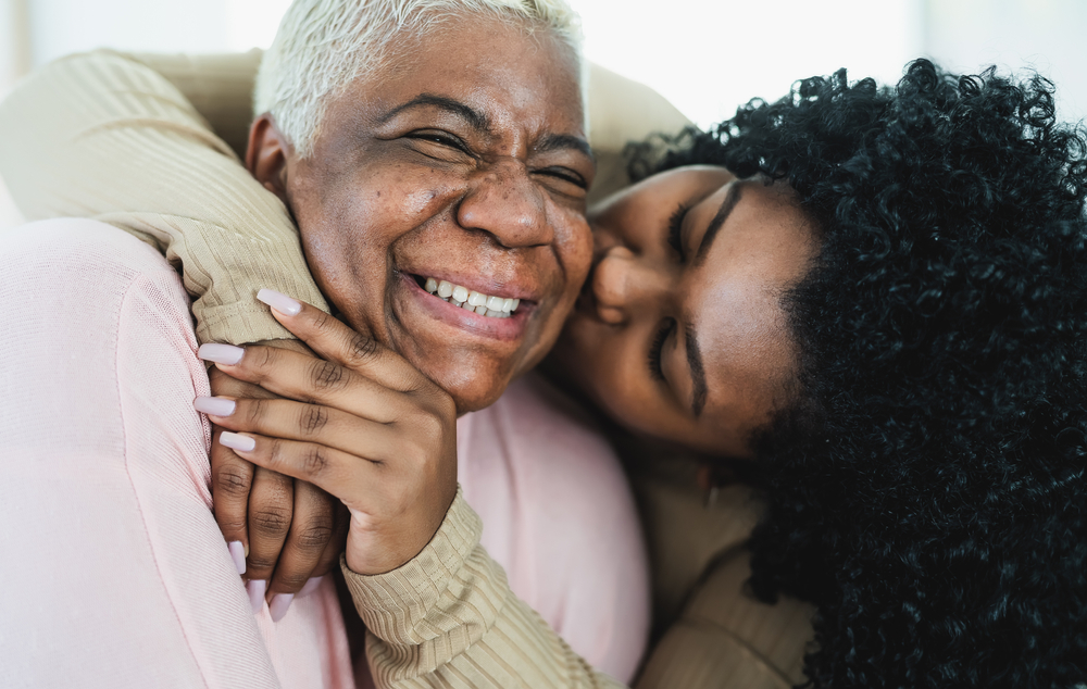 Adult daughter kissing smiling mother.