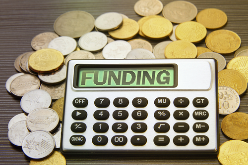 Coins surrounding a calculator with the text “FUNDING” written across its screen.