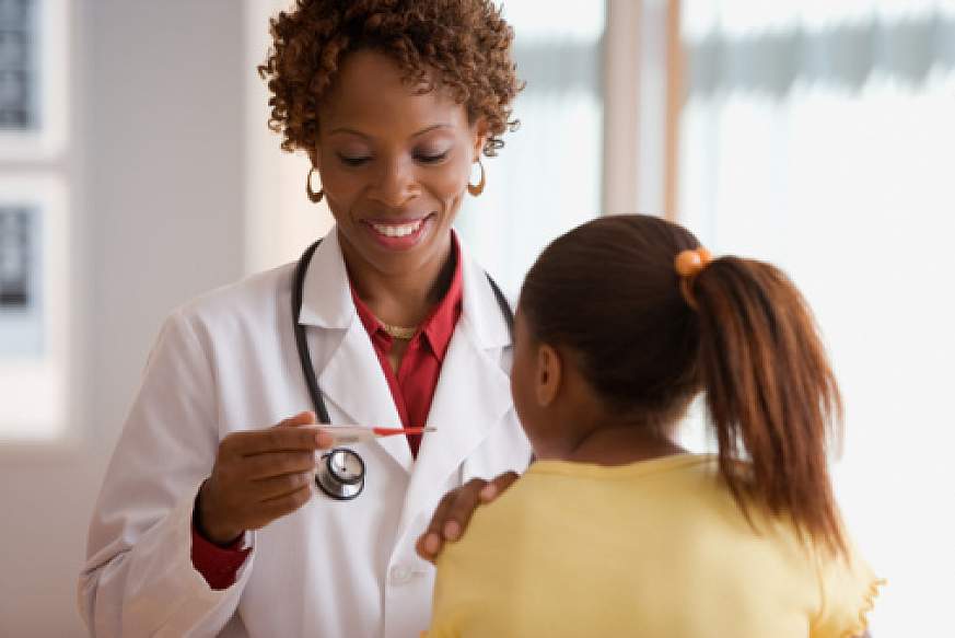 A doctor with a pleasant smile looks at the reading on a thermometer. Her hand is on the patient's shoulder.