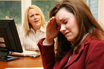 Photo of business woman looking stressed with an angry business woman in the background