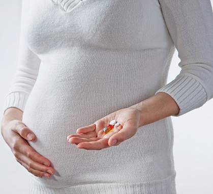 Photo of a pregnant woman holding vitamins in front of her belly Photo of a pregnant woman holding vitamins in front of her belly