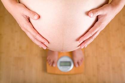 Photo of a pregnant woman on a scale holding her belly. Photo of a pregnant woman on a scale holding her belly