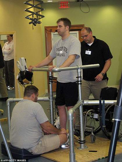 Photo of a standing man supported by hand rails and physical therapists Photo of a standing man supported by hand rails and physical therapists