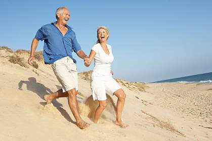 An older couple running down a sand dune An older couple running down a sand dune.