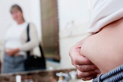 Woman looking at her reflection in a bathroom mirror and pinching her stomach fat Woman looking at her reflection in a bathroom mirror and pinching her stomach fat.