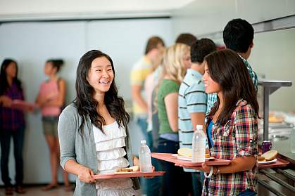 teenage girl listening to a friend in a noisy cafeteria.