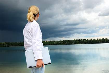 Woman with a laptop looking over a lake as a heavy storm approaches Woman with a laptop looking over a lake as a heavy storm approaches.