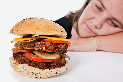 Photo of an overweight young woman resting her head on her arm and gazing longingly at a forbidden cheeseburger. Photo of an overweight young woman resting her head on her arm and gazing longingly at a forbidden cheeseburger.