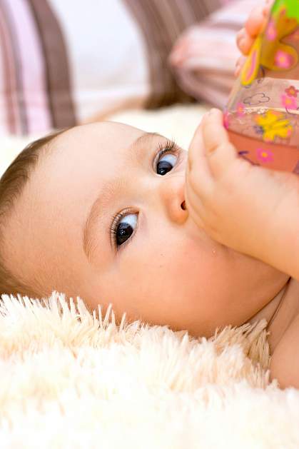 Infant watching someone while drinking from a bottle. Infant watching someone while drinking from a bottle.