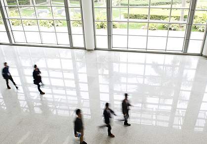Office workers walking in front of large windows with a view of outdoor gardens Office workers walking in front of large windows with a view of outdoor gardens.
