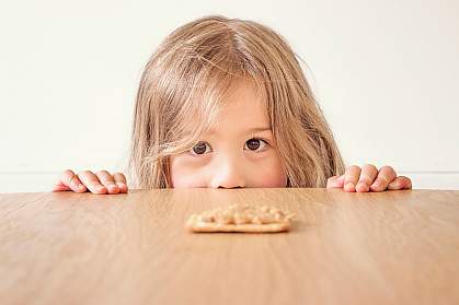 Young girl staring a peanut butter cracker on the table Young girl staring a peanut butter cracker on the table