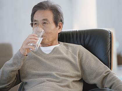 Senior man in an armchair drinking a glass of water Senior man in an armchair drinking a glass of water