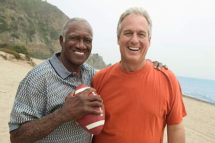 Older men, one black and one white, with a football on the beach. Older men, one black and one white, with a football on the beach