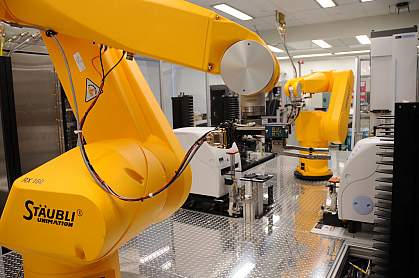 A robot arm retrieving assay plates from incubators A robot arm (foreground) retrieves assay plates from incubators to place them at compound transfer stations or hand them off to another arm (background).