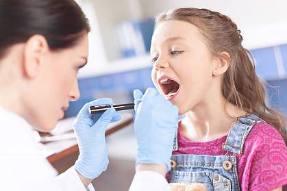Woman doctor examining girl’s throat with spatula and flashlight Woman doctor examining girl’s throat with spatula and flashlight