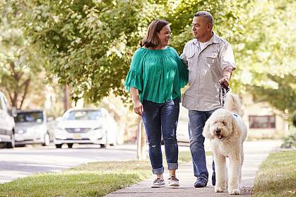 Senior couple walking dog along suburban street