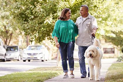 Senior couple walking dog along suburban street Senior couple walking dog along suburban street