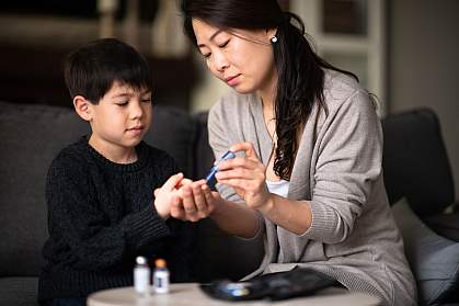 Mother helping son check blood sugar level Mother helping son check blood sugar level