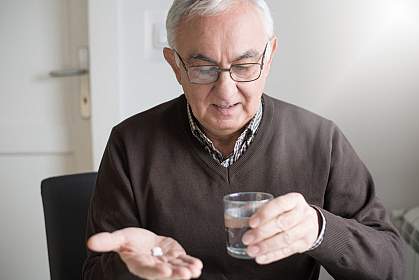 Elderly man with medicine Elderly man looking at medicine and glass of water in his hands