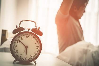 Man stretching out after waking up with alarm clock showing six ’o clock.