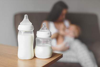 Bottles of breast milk with mother breastfeeding baby in the background Bottles of breast milk with mother breastfeeding baby in the background