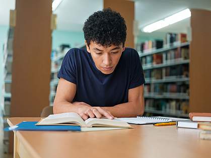 Student studying a book in the library Student studying a book in the library