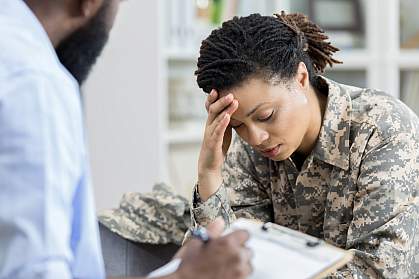 Female military veteran holding her head in an appointment with a health professional Female military veteran holding her head in an appointment with a health professional