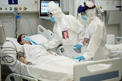 Medical team in protective equipment checking on female patient in hospital bed Medical team in protective equipment checking on female patient who is lying in a hospital bed wearing a surgical mask over a breathing device