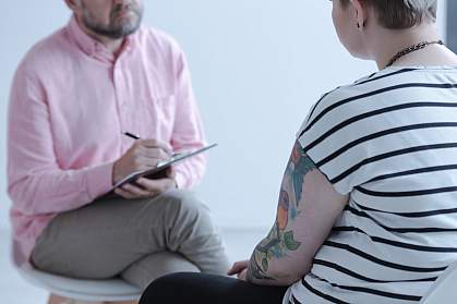 Therapist taking notes while listening to a tattooed young person Therapist taking notes while listening to a tattooed young person