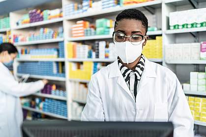 Female pharmacist with face mask at a computer Female pharmacist with face mask at a computer