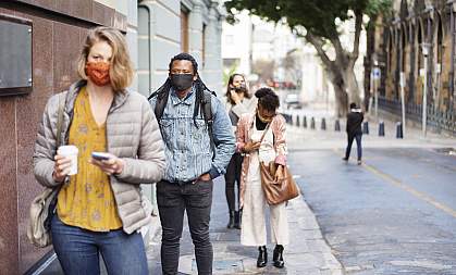Diverse group of people wearing protective face masks practicing social distancing while waiting in a line on a city sidewalk Diverse group of people wearing protective face masks practicing social distancing while waiting in a line on a city sidewalk