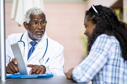 A senior black doctor explaining something on a tablet to a young black woman A senior black doctor explaining something on a tablet to a young black womanA senior black doctor explaining something on a tablet to a young black woman