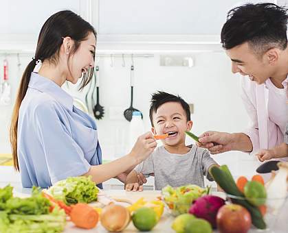 Parents with young boy eating vegetables in the kitchen Parents with young boy eating vegetables in the kitchen