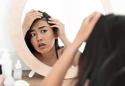 Troubled young Asian woman checking for thinning hair in mirror Troubled young Asian woman checking for thinning hair in mirror