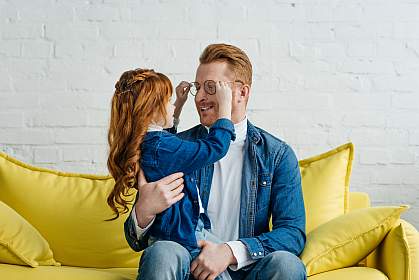 Red-haired daughter and father playing with his glasses while sitting on sofa Red-haired daughter and father playing with his glasses while sitting on sofa