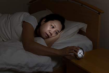 Woman in bed with eyes open touching clock on nightstand Woman in bed with eyes open touching clock on nightstand
