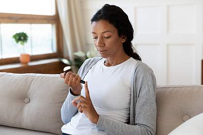 African American woman measuring blood sugar level on couch African American woman measuring blood sugar level on couch