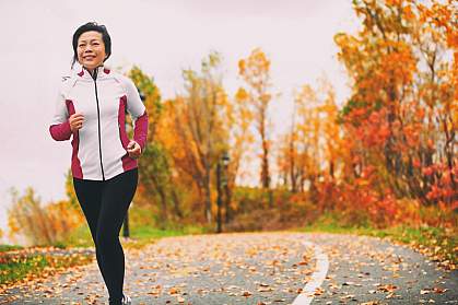 Mature Asian woman running in a park among colorful fall foliage Mature Asian woman running in a park among colorful fall foliage
