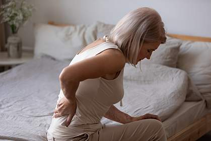 Mature woman sitting in bed holding her lower back Mature woman sitting in bed holding her lower back