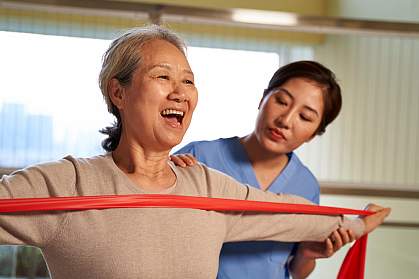 Woman using resistance band guided by physical therapist in rehab center