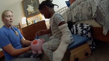Girl with a cast on one arm grasping a piece from a plastic pig using the other hand Girl with a cast on one arm grasping a piece from a plastic pig using the other hand