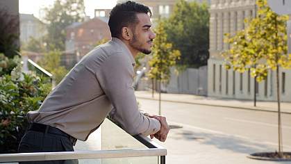 Businessman standing at balcony railing and looking down on a city street Businessman standing at balcony railing and looking down on a city street