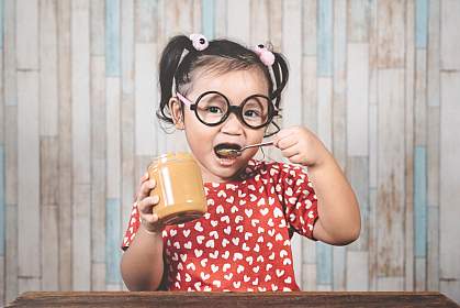 Young Asian girl holding a jar of peanut butter and putting a spoon in her mouth Young Asian girl holding a jar of peanut butter and putting a spoon in her mouth